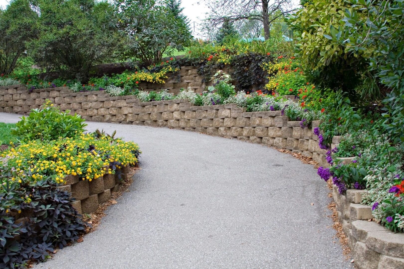 A curved driveway with stone walls and flowers.